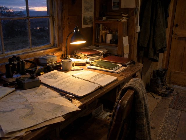 A field desk and lamp inside the cabin at dusk